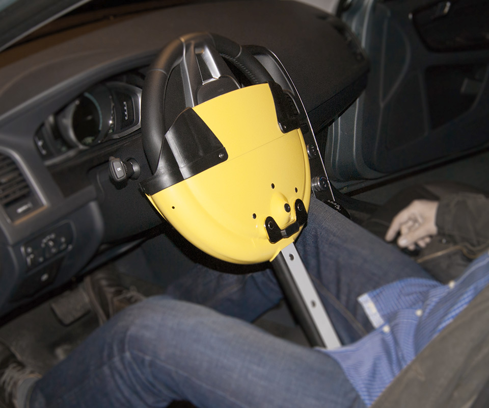 Lenkradkralle Autolock (gelb) am Lenkrad eines Volvo XC-60 montiert, Blockierung an den beinen des Fahrers